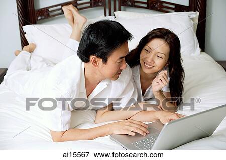 Couple lying side by side on bed, using laptop View Large Photo Image Stock Photo - Couple lying side by side on bed, using laptop. Fotosearch