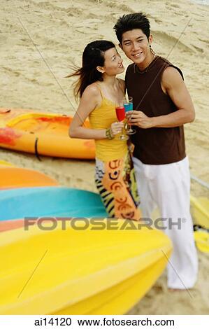 Stock Image - Couple on beach, holding drinks, looking away. Fotosearch
