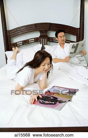 Couple on bed, woman reading magazine, man reading newspaper View Large Photo Image Stock Photo - Couple on bed, woman reading magazine, man reading newspaper. Fotosearch