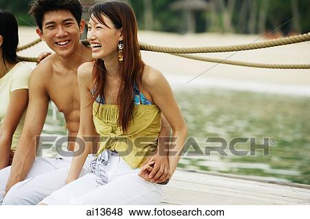 Couple on jetty, sitting side by side View Large Photo Image Stock Photo - Couple on jetty, sitting side by side. Fotosearch