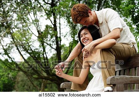 Couple on park bench, man sitting behind woman, holding her hands View Large Photo Image Stock Image - Couple on park bench, man sitting behind woman, holding her hands. Fotosearch