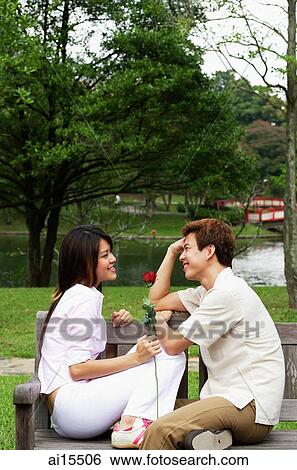 Stock Photograph - Couple on park bench, sitting face to face, woman holding a rose. Fotosearch