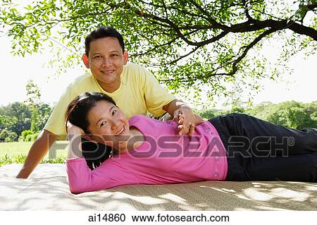 Stock Image - Couple on picnic mat, woman lying down, man sitting behind her. Fotosearch