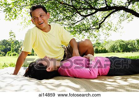 Stock Photo - Couple on picnic mat, woman lying down, man sitting looking away. Fotosearch