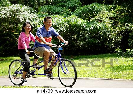 Couple riding tandem bicycle in park View Large Photo Image Stock Photo - Couple riding tandem bicycle in park. Fotosearch