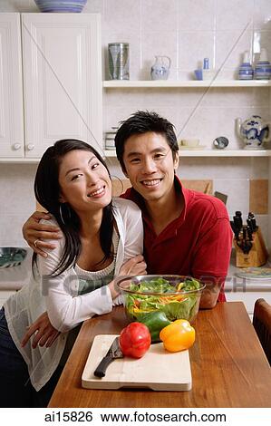 Stock Photograph - Couple side by side in kitchen, smiling at camera. Fotosearch