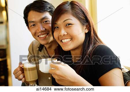 Couple sitting, holding coffee cups, smiling at camera View Large Photo Image Picture - Couple sitting, holding coffee cups, smiling at camera. Fotosearch