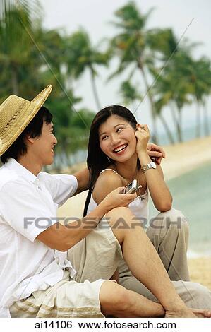 Couple sitting on beach, man holding mobile phone View Large Photo Image Stock Photograph - Couple sitting on beach, man holding mobile phone. Fotosearch