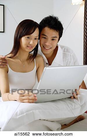 Couple sitting on bed, using laptop View Large Photo Image Stock Image - Couple sitting on bed, using laptop. Fotosearch