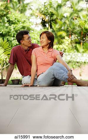 Couple sitting on floor, side by side, looking at each other View Large Photo Image Stock Image - Couple sitting on floor, side by side, looking at each other. Fotosearch
