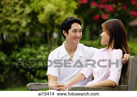 Couple sitting on park bench, holding hands, looking at each other View Large Photo Image Picture - Couple sitting on park bench, holding hands, looking at each other. Fotosearch