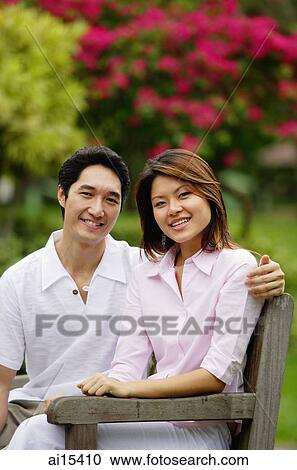 Couple sitting on park bench, looking at camera View Large Photo Image Stock Image - Couple sitting on park bench, looking at camera. Fotosearch