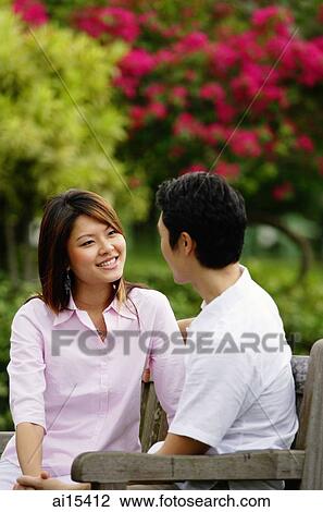 Couple sitting on park bench, looking at each other View Large Photo Image Stock Image - Couple sitting on park bench, looking at each other. Fotosearch