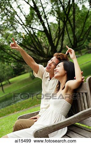 Couple sitting on park bench, looking up, man pointing View Large Photo Image Stock Photo - Couple sitting on park bench, looking up, man pointing. Fotosearch