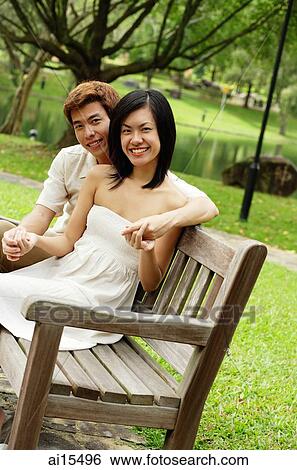 Couple sitting on park bench, looking at camera View Large Photo Image Stock Photograph - Couple sitting on park bench, looking at camera. Fotosearch