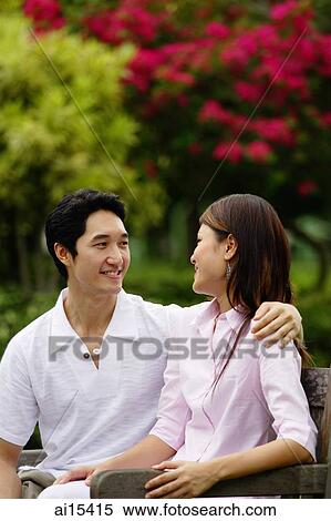 Couple sitting on park bench, looking at each other, smiling View Large Photo Image Stock Photography - Couple sitting on park bench, looking at each other, smiling. Fotosearch