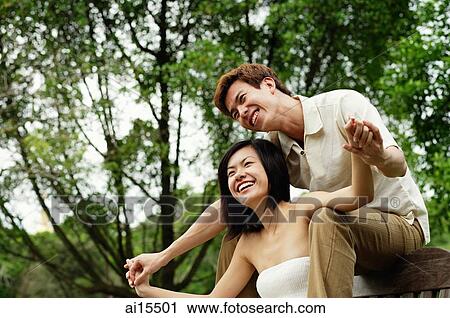 Couple sitting on park bench, man sitting behind woman, holding her hands View Large Photo Image Stock Image - Couple sitting on park bench, man sitting behind woman, holding her hands. Fotosearch