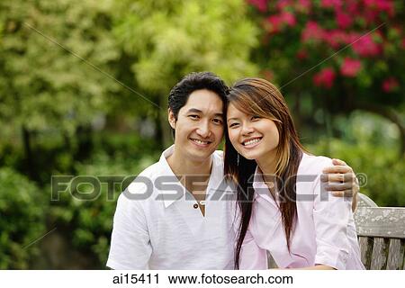 Couple sitting on park bench, smiling at camera View Large Photo Image Stock Image - Couple sitting on park bench, smiling at camera. Fotosearch