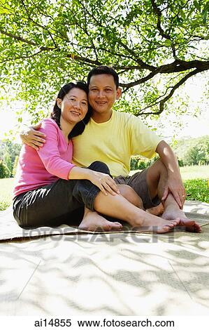 Stock Photography - Couple sitting on picnic mat, looking at camera. Fotosearch