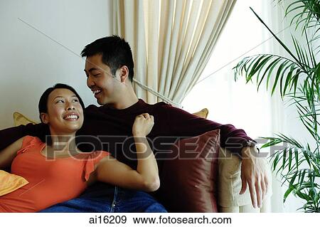 Stock Photo - Couple sitting on sofa, woman leaning on man, looking up at him. Fotosearch