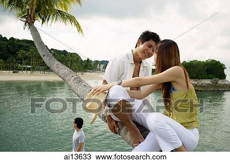 Stock Image - Couple sitting on tree, face to face. Fotosearch