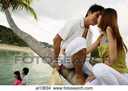 Couple sitting on tree, kissing, another couple standing in the background View Large Photo Image Picture - Couple sitting on tree, kissing, another couple standing in the background. Fotosearch
