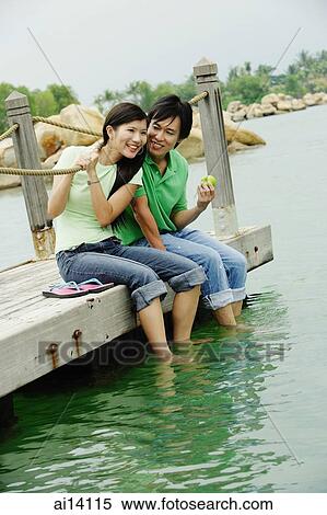 Stock Photography - Couple sitting side by side on jetty. Fotosearch