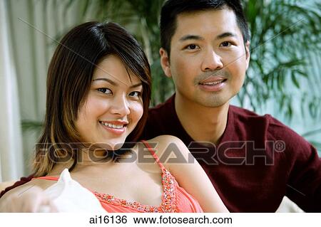 Stock Photograph - Couple sitting side by side, smiling at camera. Fotosearch