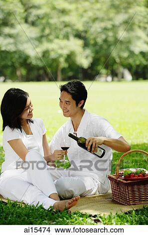Couple sitting with picnic basket, smiling at each other, man pouring wine from bottle View Large Photo Image Picture - Couple sitting with picnic basket, smiling at each other, man pouring wine from bottle. Fotosearch