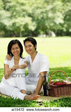 Stock Image - Couple sitting with picnic basket, smiling at camera. Fotosearch
