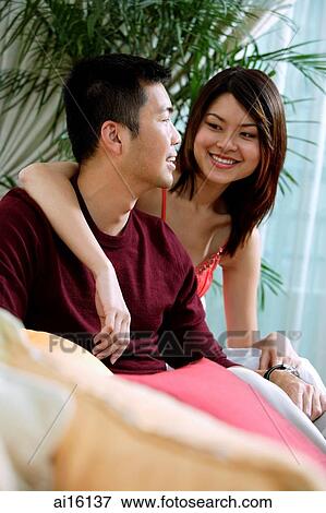 Stock Photo - Couple sitting, woman with arm around man. Fotosearch