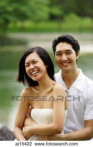 Couple smiling at camera, man hugging woman from behind View Large Photo Image Stock Image - Couple smiling at camera, man hugging woman from behind. Fotosearch