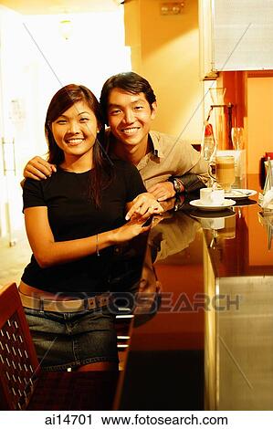 Stock Image - Couple standing at bar counter, looking at camera, portrait. Fotosearch