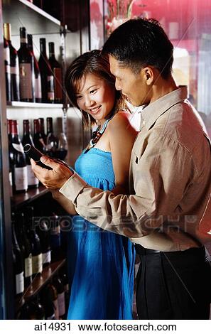 Couple standing in front of shelf holding wine bottles View Large Photo Image Stock Image - Couple standing in front of shelf holding wine bottles. Fotosearch