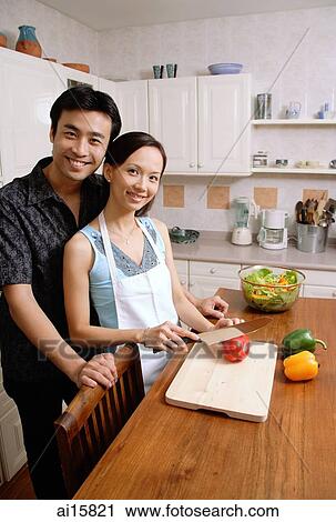 Stock Image - Couple standing in kitchen, woman chopping vegetables, smiling at camera. Fotosearch