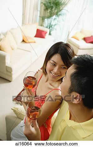Picture - Couple standing in living room, holding drinks. Fotosearch