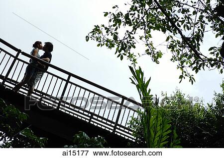 Stock Photo - Couple standing next to railing, kissing, low angle view. Fotosearch