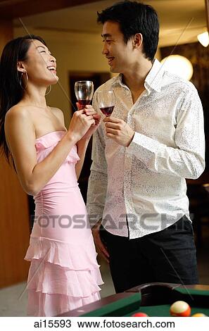 Stock Image - Couple standing side by side, holding wine glasses. Fotosearch