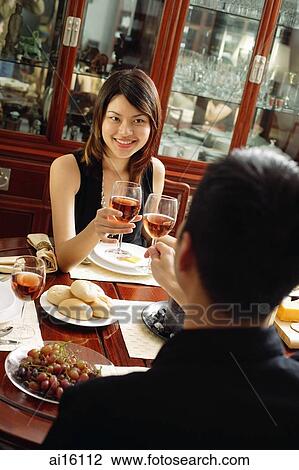 Stock Image - Couple toasting wine glasses across dining table. Fotosearch