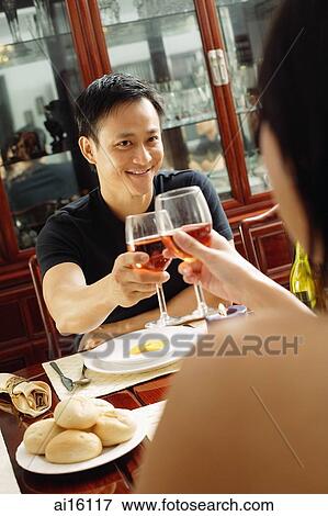 Stock Photo - Couple toasting with wine glasses across dining table. Fotosearch