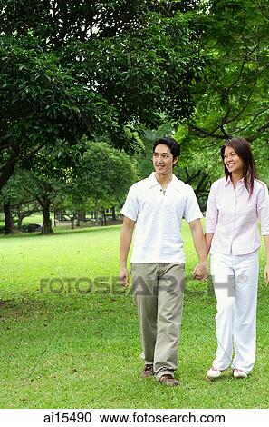 Stock Image - Couple walking across park, holding hands. Fotosearch