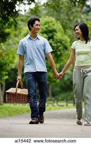 Couple walking hand in hand in park, man carrying picnic basket View Large Photo Image Stock Image - Couple walking hand in hand in park, man carrying picnic basket. Fotosearch