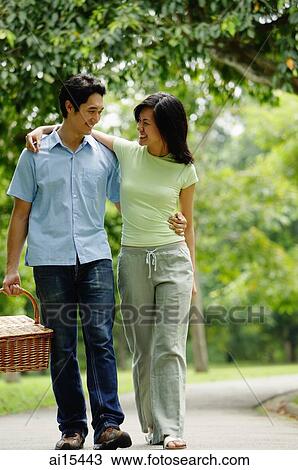 Stock Image - Couple walking in park, man carrying picnic basket. Fotosearch