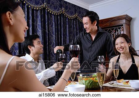 Stock Photograph - Couples having dinner party at home, man pouring wine for man. Fotosearch