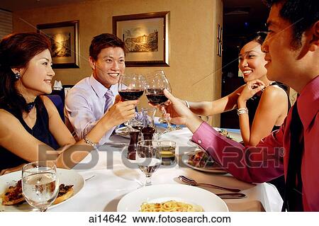 Stock Image - Couples in restaurant, toasting with wine glasses. Fotosearch