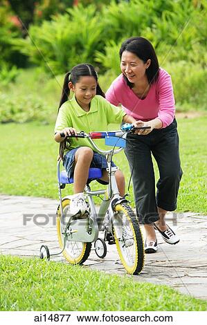 Daughter cycling, mother guiding her View Large Photo Image Stock Photo - Daughter cycling, mother guiding her. Fotosearch