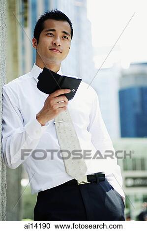 Stock Image - Executive holding PDA, leaning on wall, looking away. Fotosearch