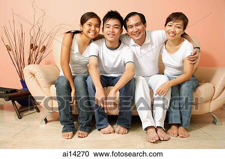 Stock Image - Family of four in living room, looking at camera, portrait. Fotosearch
