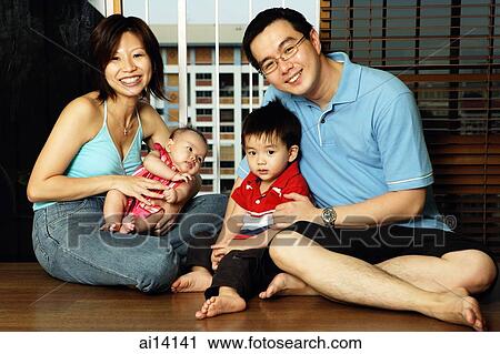 Stock Image - Family portrait, family with two children sitting on floor, looking at camera. Fotosearch