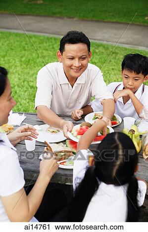 Family sitting at picnic table, father passing daughter food View Large Photo Image Stock Image - Family sitting at picnic table, father passing daughter food. Fotosearch